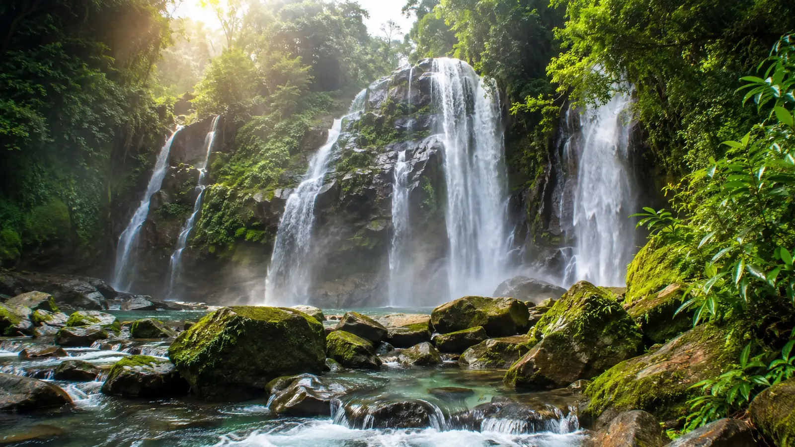 Cascadas anchas cayendo entre vegetación selvática iluminada por rayos de sol.