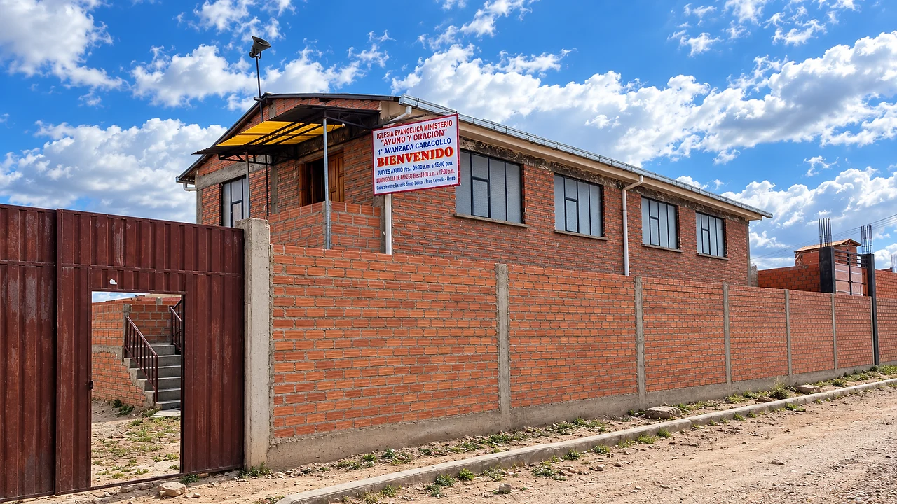 El templo de Caracollo desde la calle: muro de ladrillo, portón metálico y el letrero de bienvenida sobre la fachada